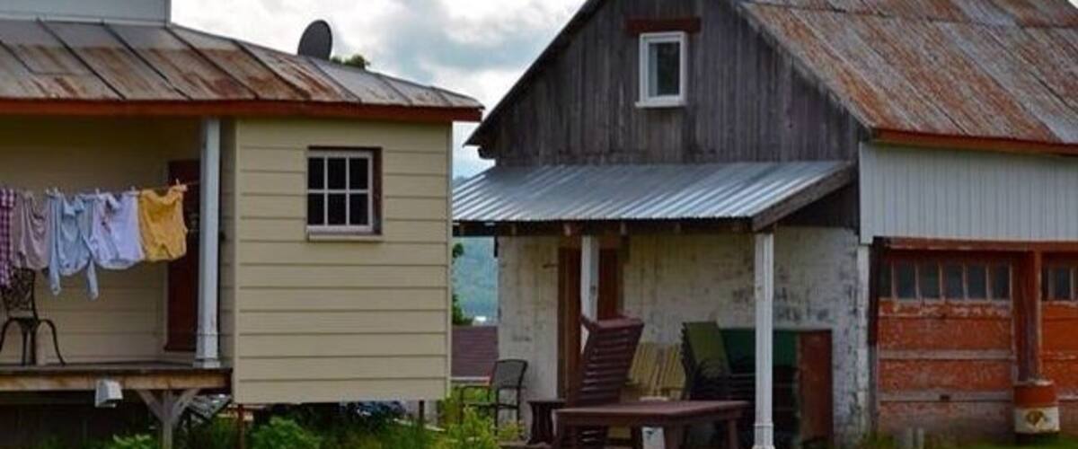 A rustic wooden house with a porch and a small shed.