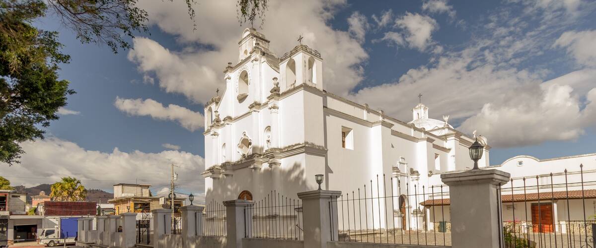 A white church with a bell tower and a fence in front.