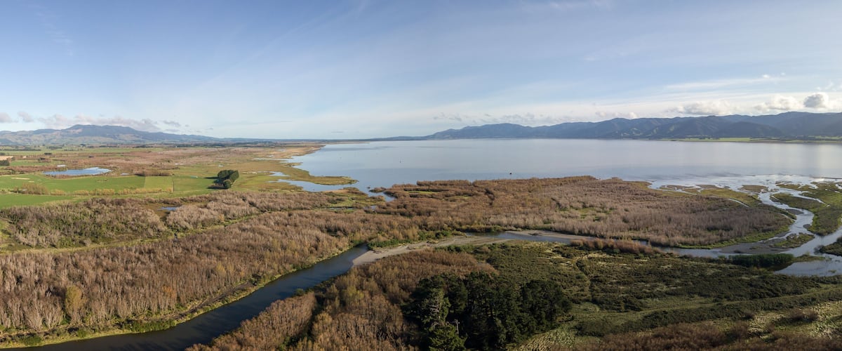 A river winding through a marshy landscape with a lake and mountains in the background.