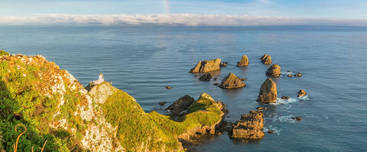 Rainbow over Nugget Point lighthouse after the storm. Ahuriri Flat, Clutha district, Otago region, South Island, New Zealand.