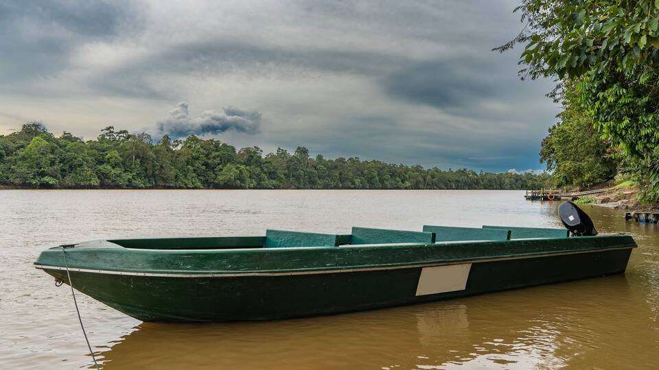 A green boat docked at a riverbank with a forested area in the background.