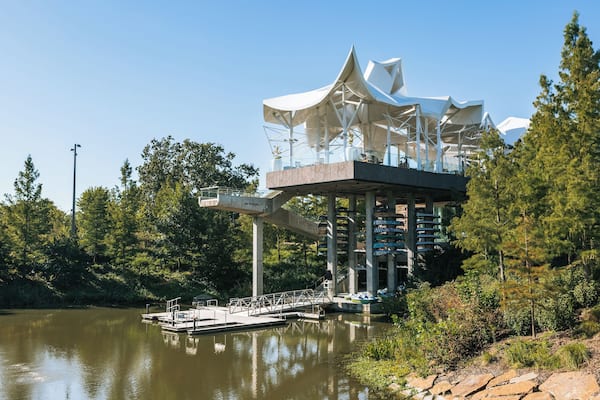 Une structure architecturale moderne au design unique, située au bord d’un plan d’eau paisible et entourée d’une végétation luxuriante.