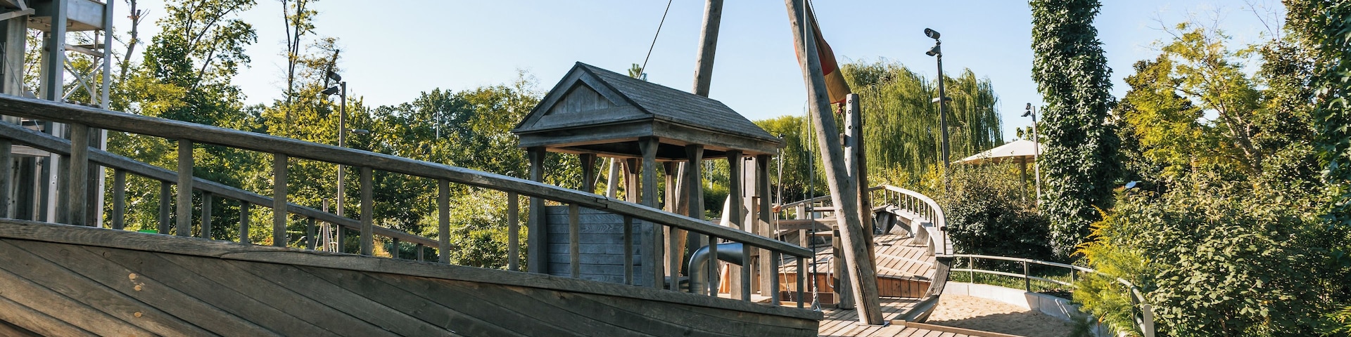 A wooden boat docked at a sandy beach with a wooden pier and a small pavilion in the background.