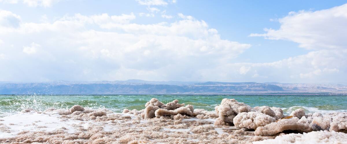 A salt flat with white salt formations in the foreground and a body of water in the background.