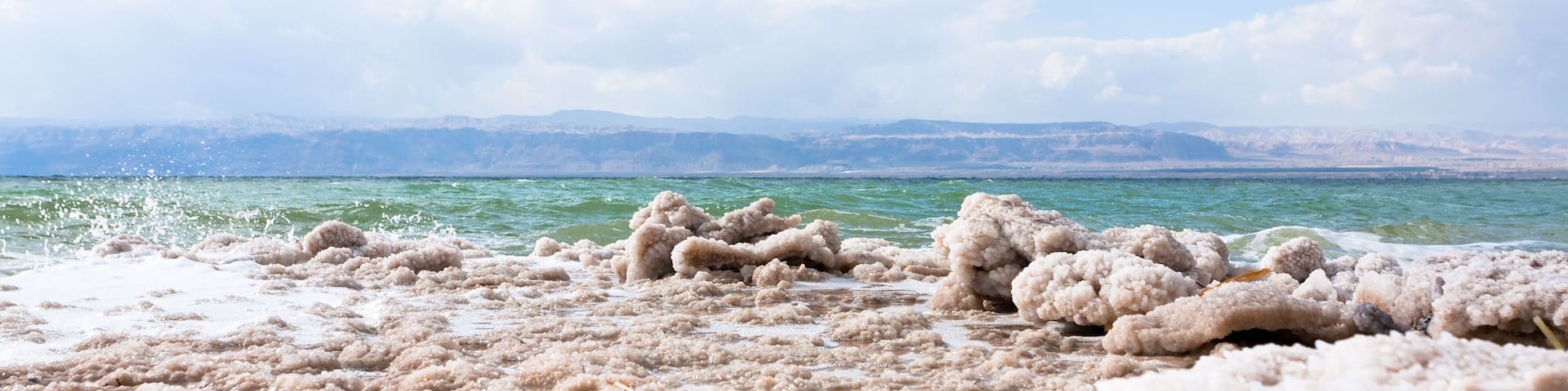 A salt flat with white salt formations in the foreground and a body of water in the background.