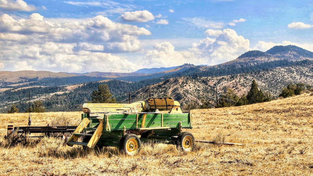 An abandoned Green and Yellow farm trailer rests on a grassy hillside in the mountains near Townsend, MT, on a sunny, summer day..
