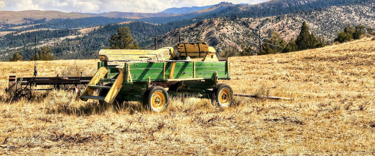 An abandoned Green and Yellow farm trailer rests on a grassy hillside in the mountains near Townsend, MT, on a sunny, summer day..