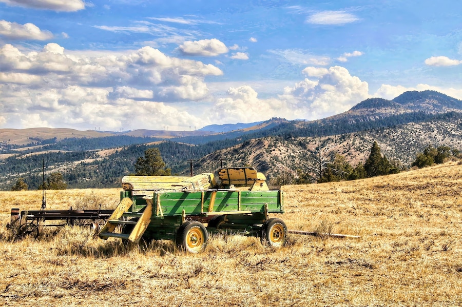 An abandoned Green and Yellow farm trailer rests on a grassy hillside in the mountains near Townsend, MT, on a sunny, summer day..