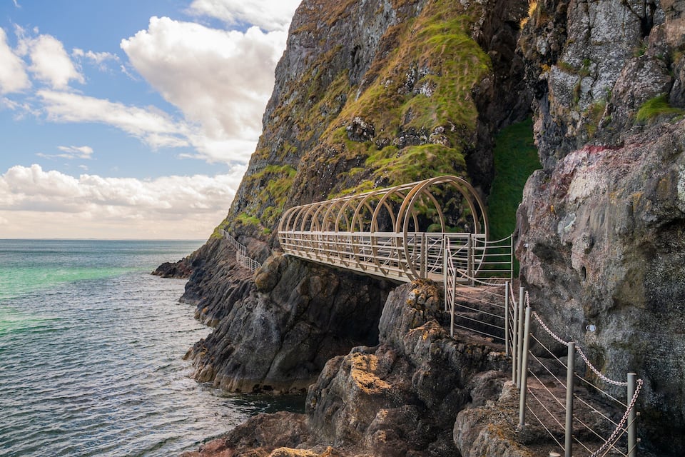 A metal bridge over a rocky cliff by the sea.