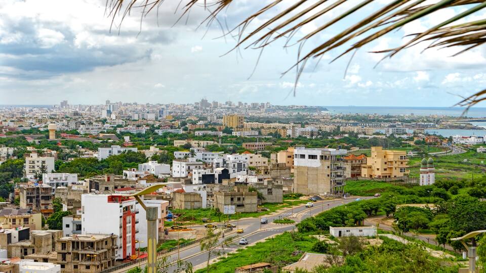 A cityscape with a mix of modern and older buildings, a road, and a body of water in the distance.