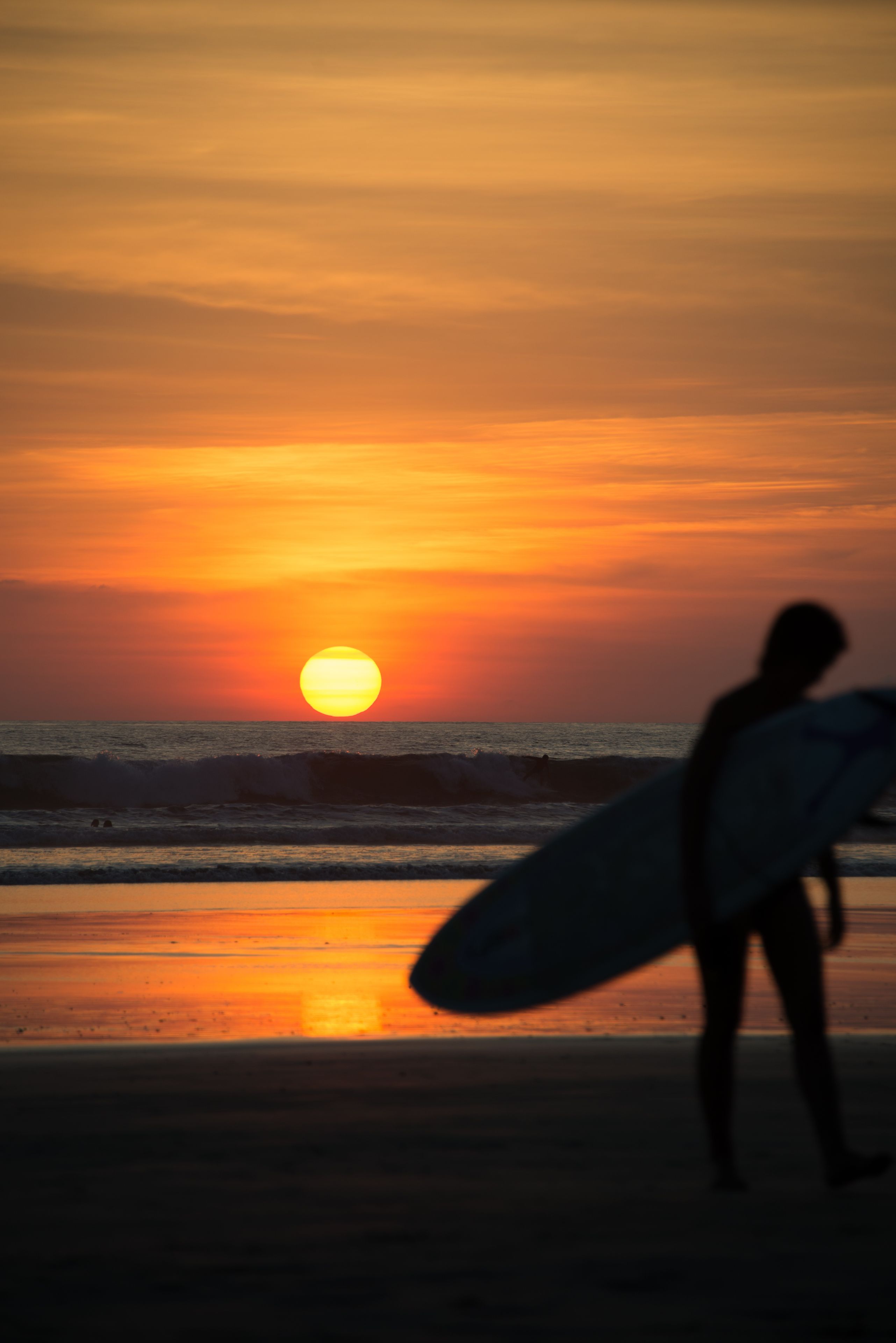 A sunset over the ocean with a silhouette of a person holding a surfboard.