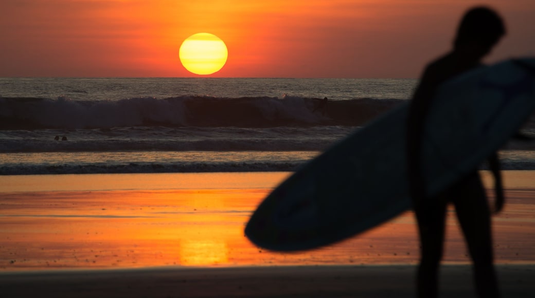 A sunset over the ocean with a silhouette of a person holding a surfboard.
