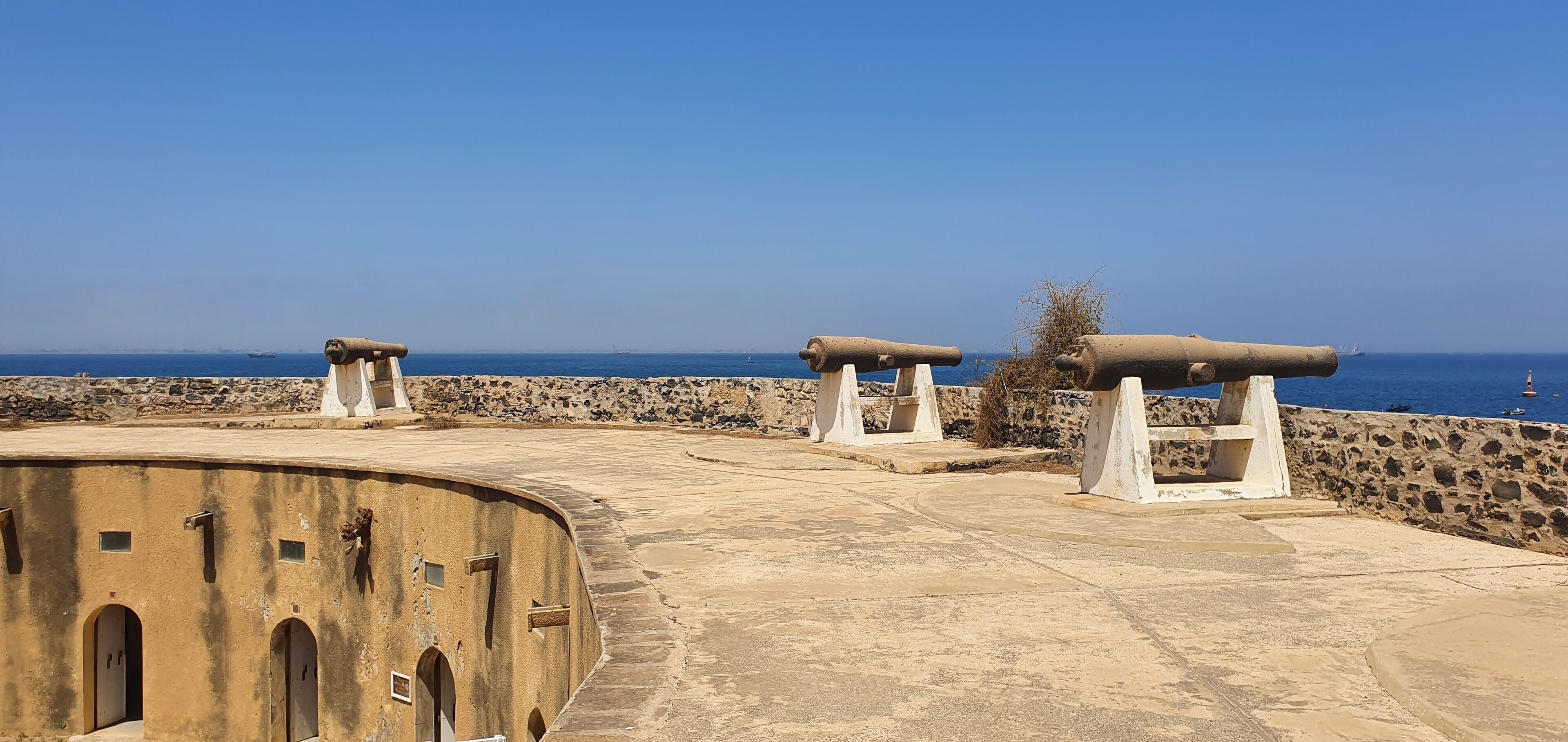 A coastal fort with cannons, a clear blue sky, and the sea in the background.