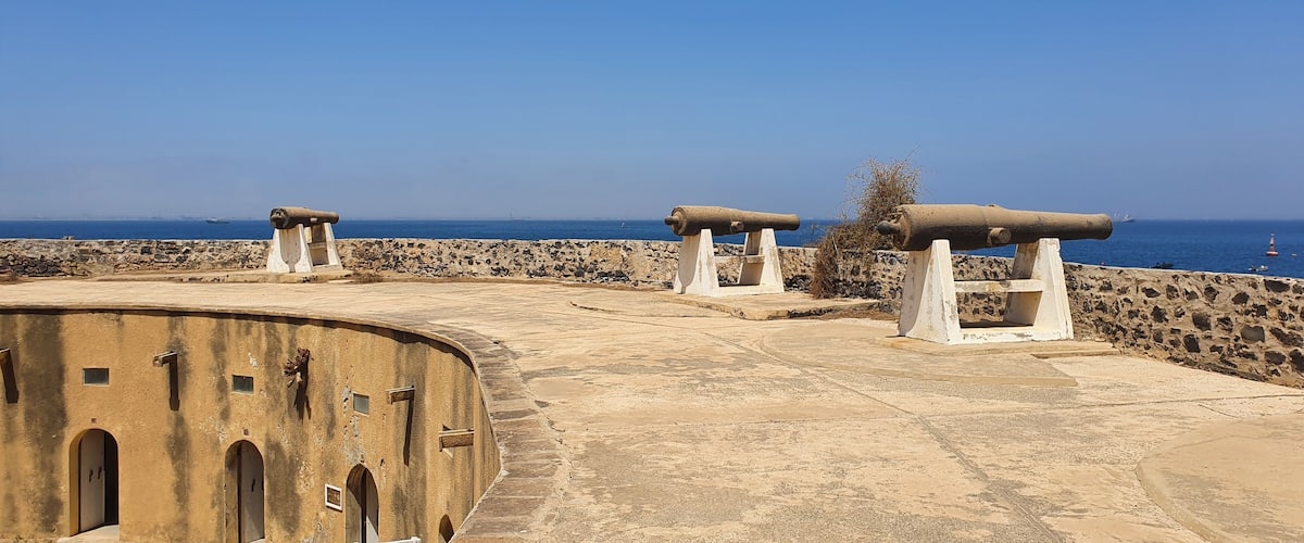 A coastal fort with cannons, a clear blue sky, and the sea in the background.