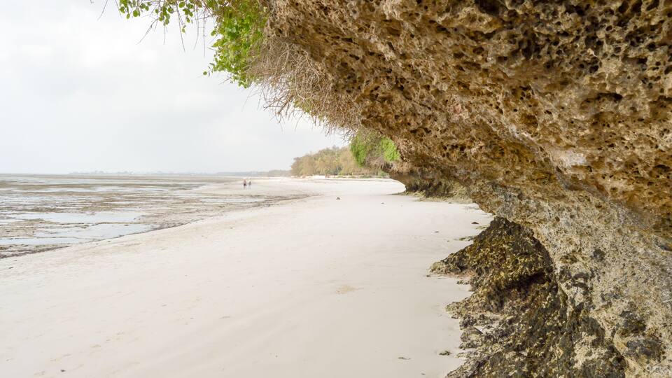 A beach with a rocky overhang and calm water.
