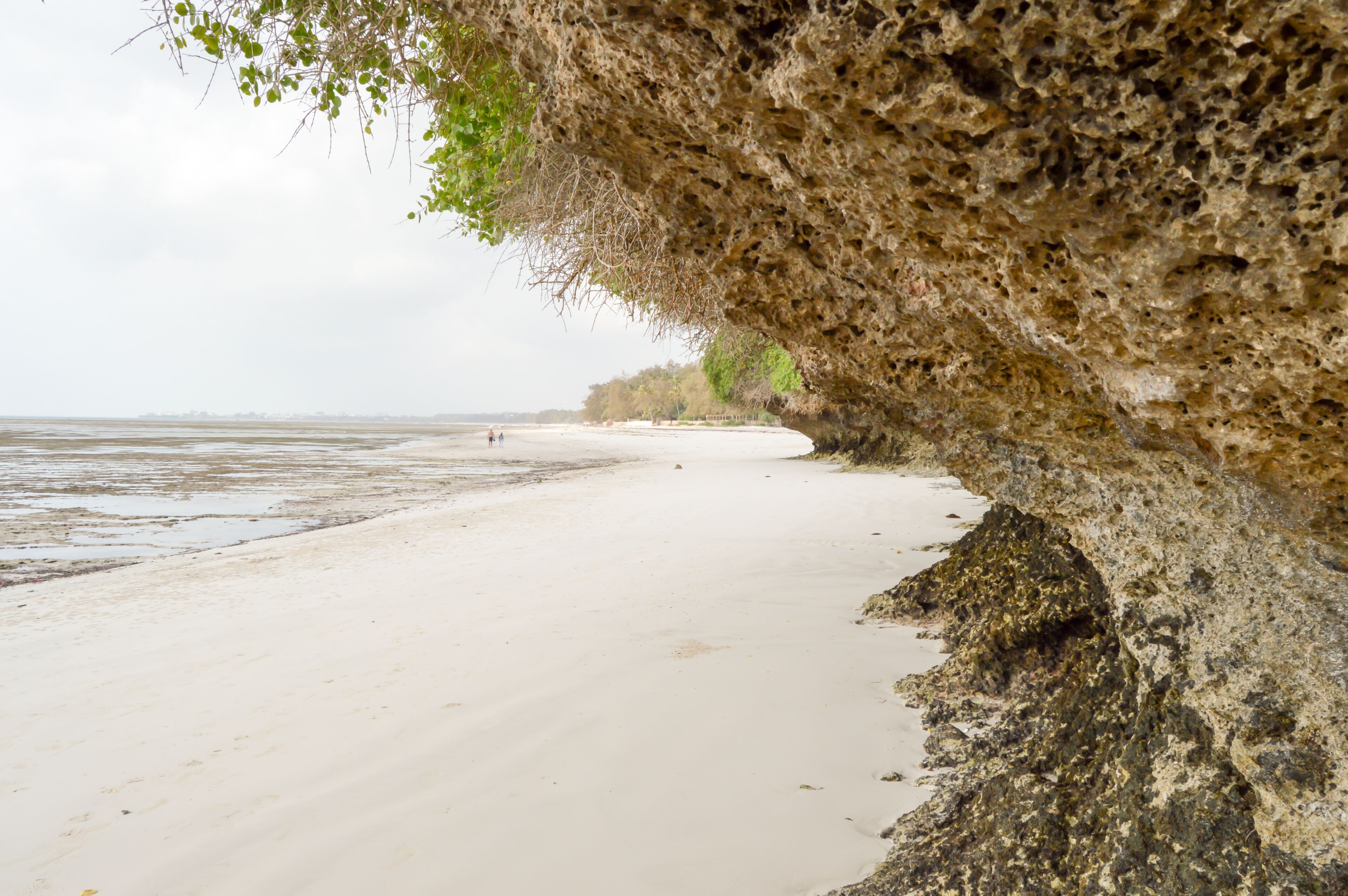A beach with a rocky overhang and calm water.
