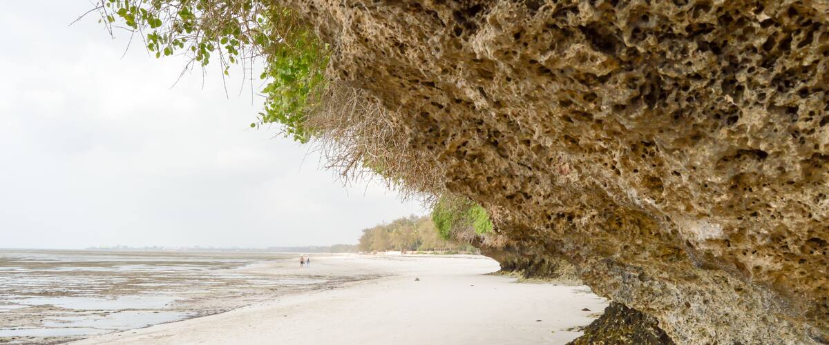 A beach with a rocky overhang and calm water.