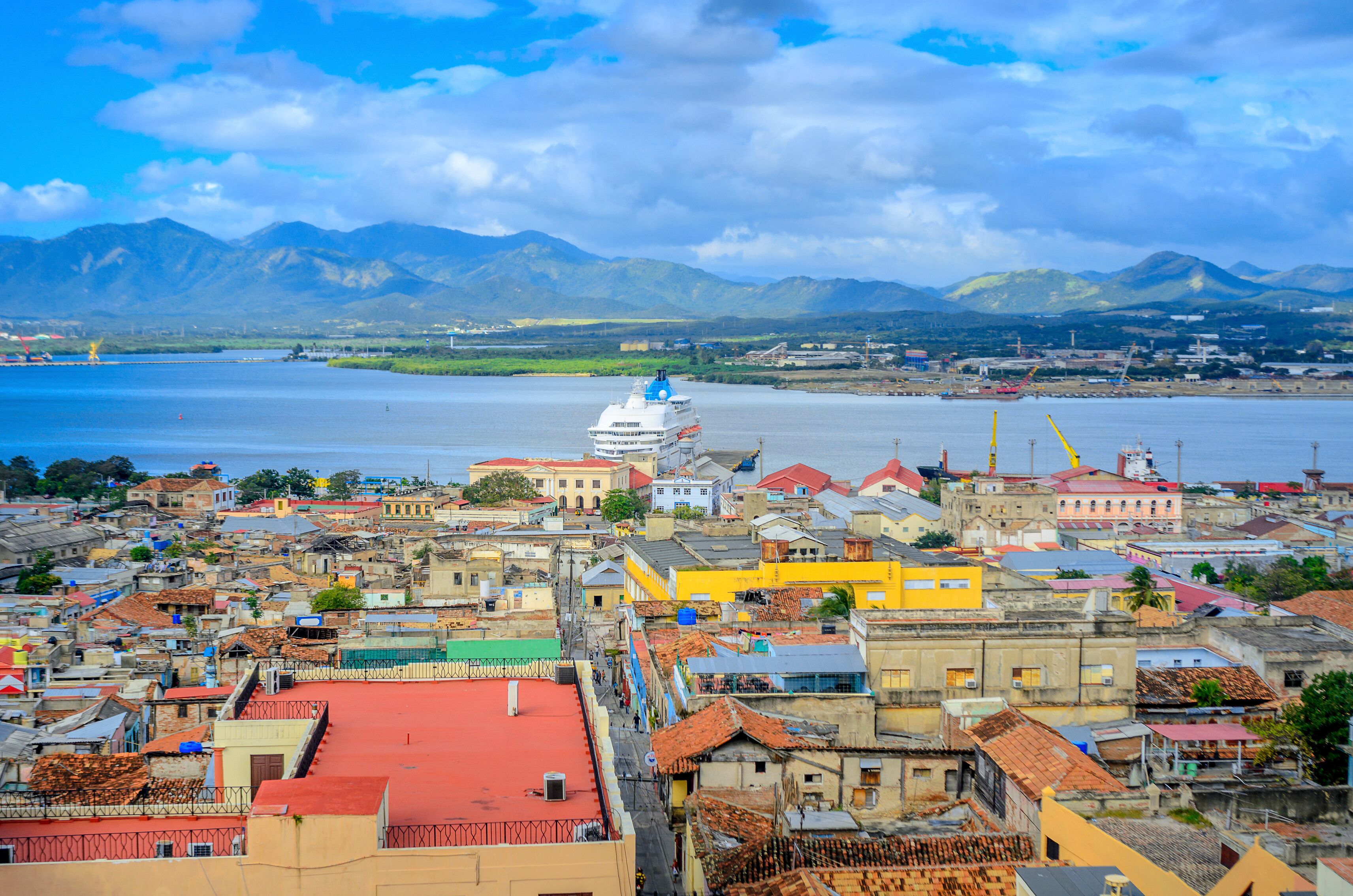 A coastal city with a prominent white dome structure, colorful buildings, and mountains in the background.