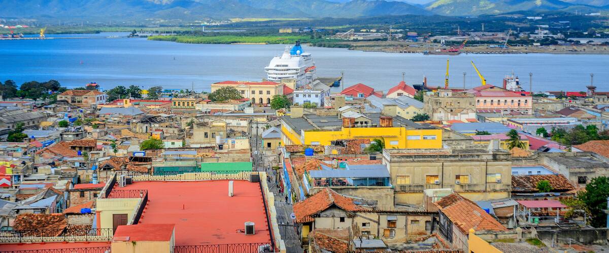 A coastal city with a prominent white dome structure, colorful buildings, and mountains in the background.