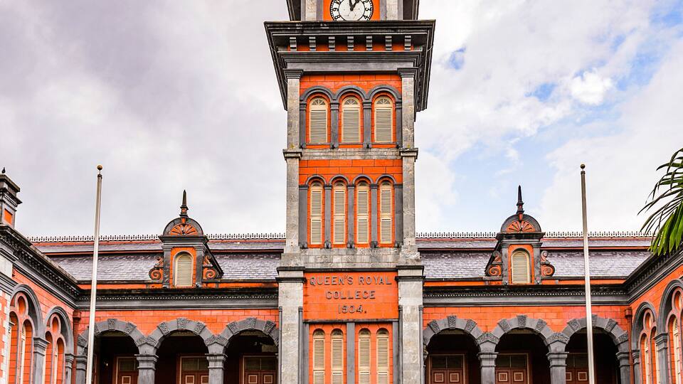 A historic building with a clock tower, arched windows, and a statue in front.