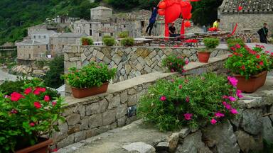 A traditional village with stone buildings, a stone wall, and potted flowers.