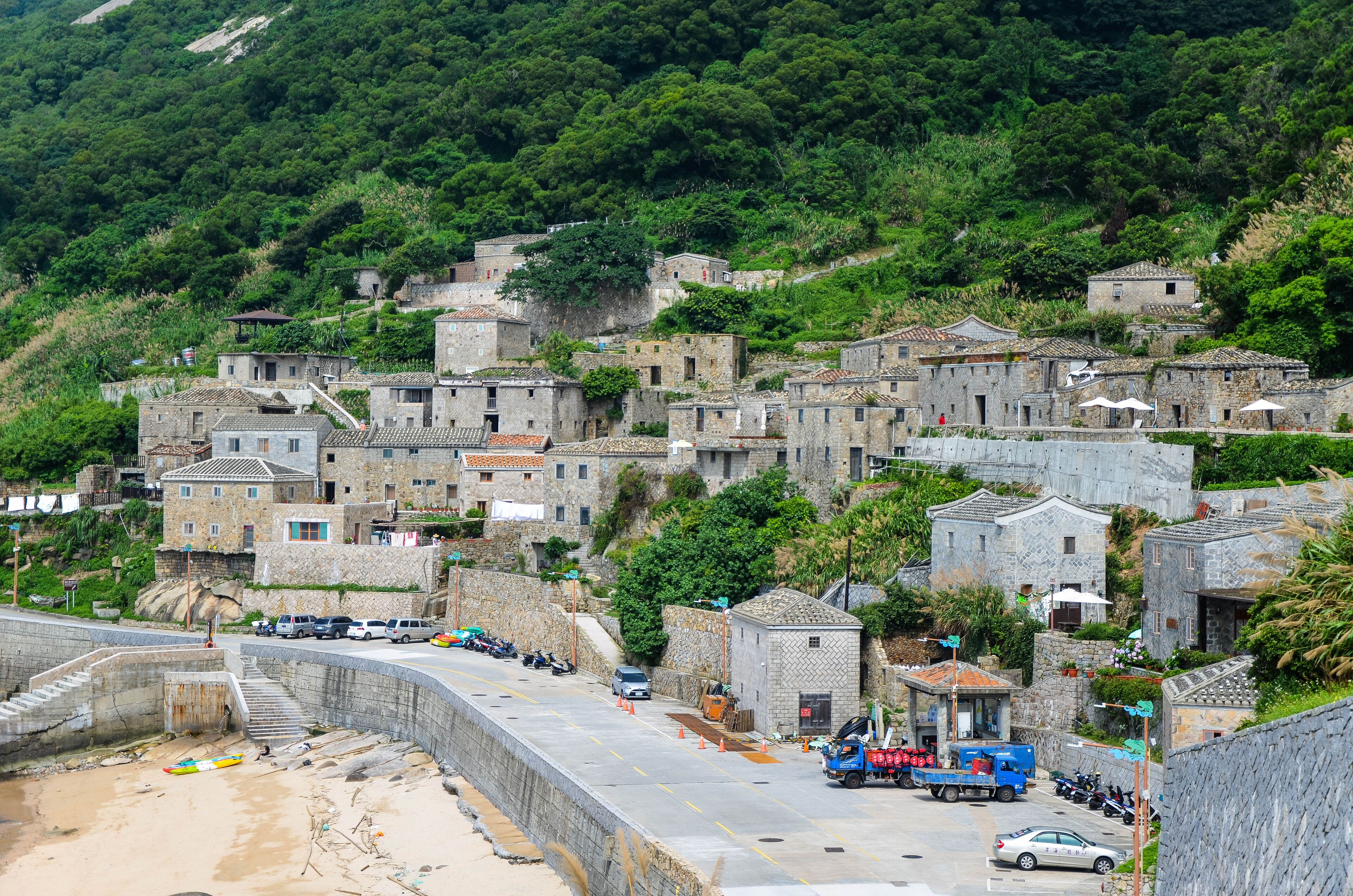 A coastal village with stone buildings, a beach, and parked vehicles.