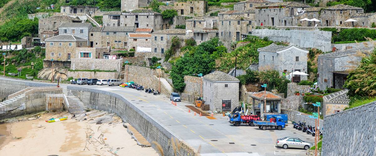 A coastal village with stone buildings, a beach, and parked vehicles.