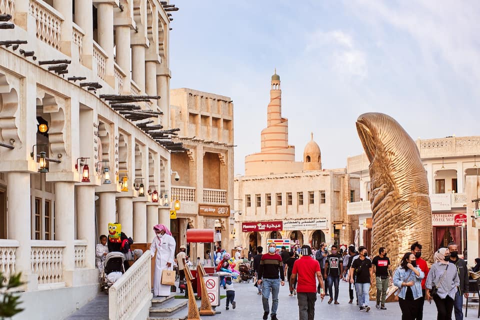 A bustling street with traditional architecture, a prominent minaret, and a large golden sculpture.