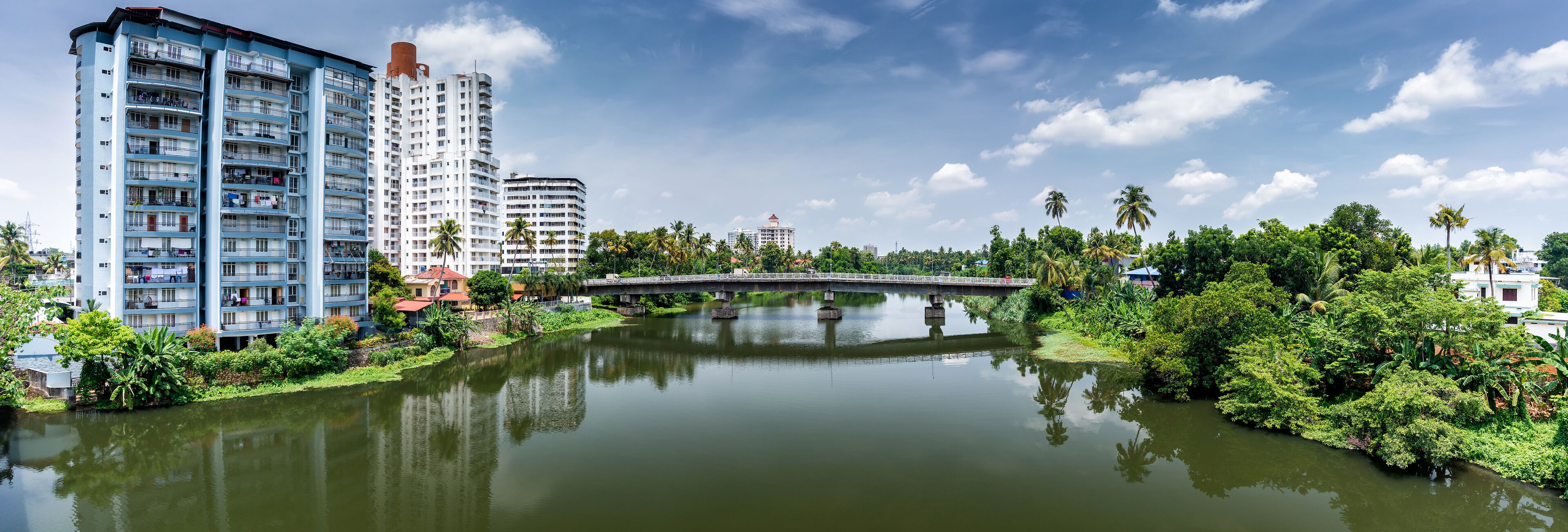 A river with a bridge, surrounded by greenery and tall buildings.