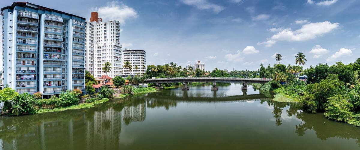 A river with a bridge, surrounded by greenery and tall buildings.