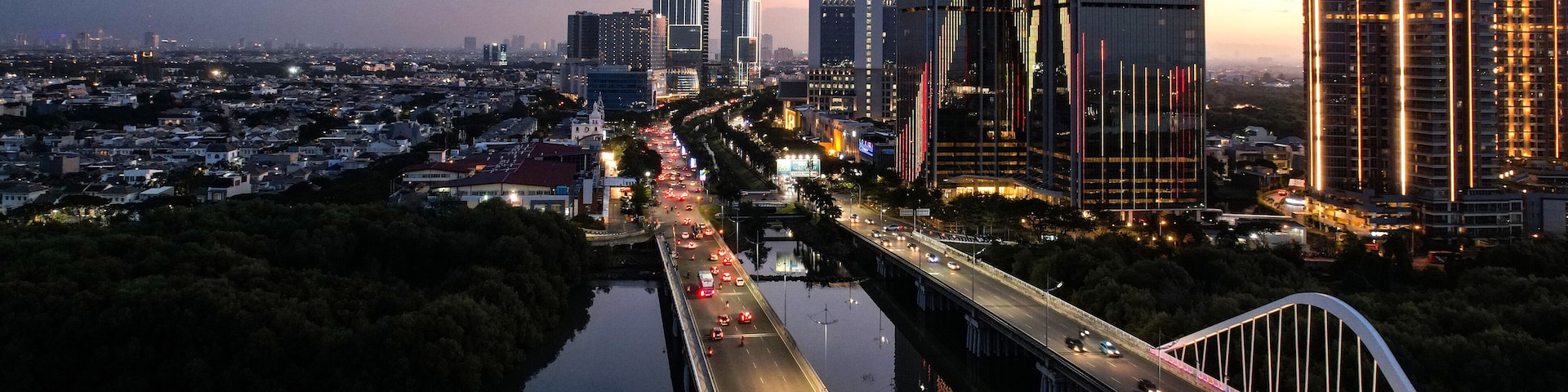 Aerial view of Pantai Indah Kapuk Avenue Bridge Jakarta. a Largest bridge in Jakarta. With Jakarta cityscape and noise cloud when sunset.