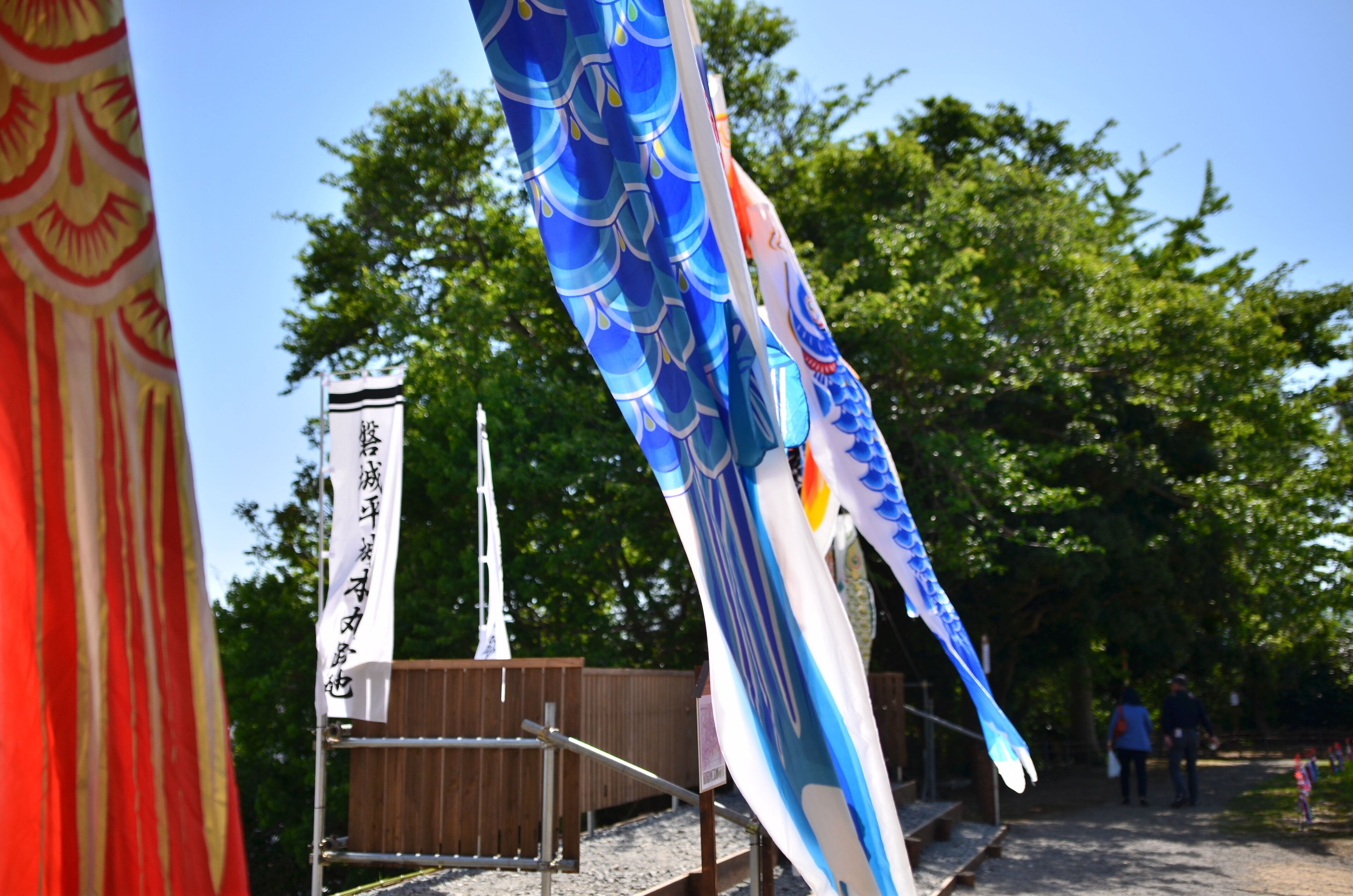 A traditional Japanese sailboat with a blue and white sail, a wooden fence, and a clear blue sky.