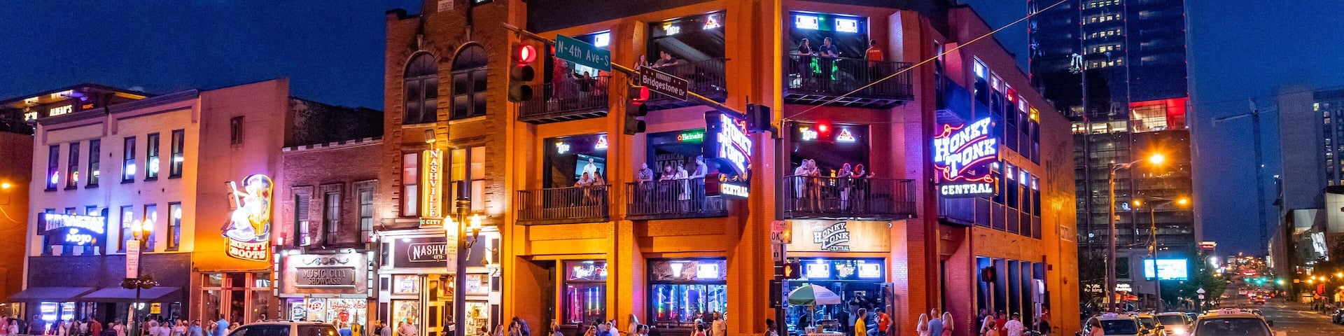 A brightly lit urban street scene at night with a multi-story building featuring neon signs and a crosswalk.