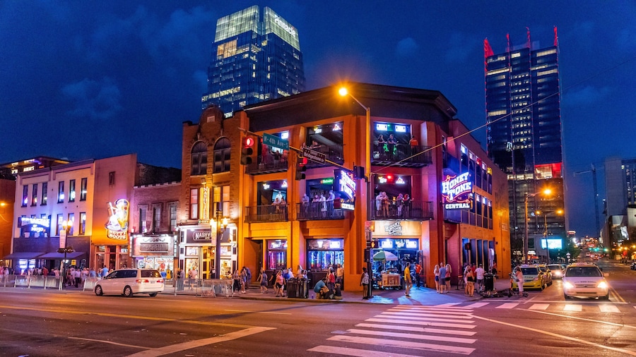 A brightly lit urban street scene at night with a multi-story building featuring neon signs and a crosswalk.