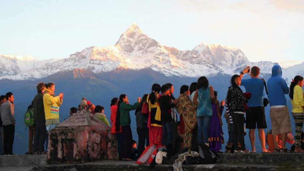 A group of people standing on a stone platform overlooking a snow-capped mountain range.