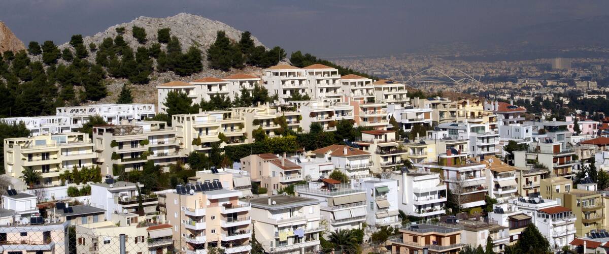 A densely packed residential area with multi-story buildings, a prominent hill with trees, and a distant cityscape.