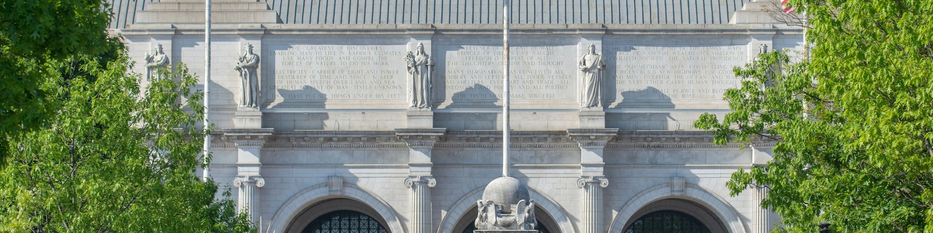A large neoclassical building with a prominent American flag, statues, and arched windows.