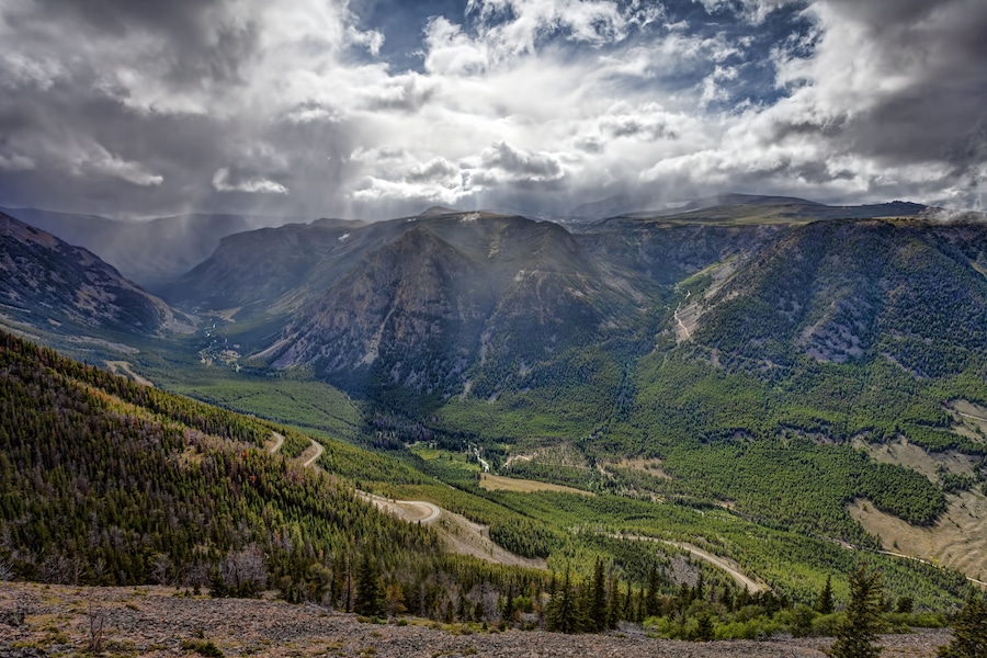 A mountainous landscape with a winding road through a dense forest.