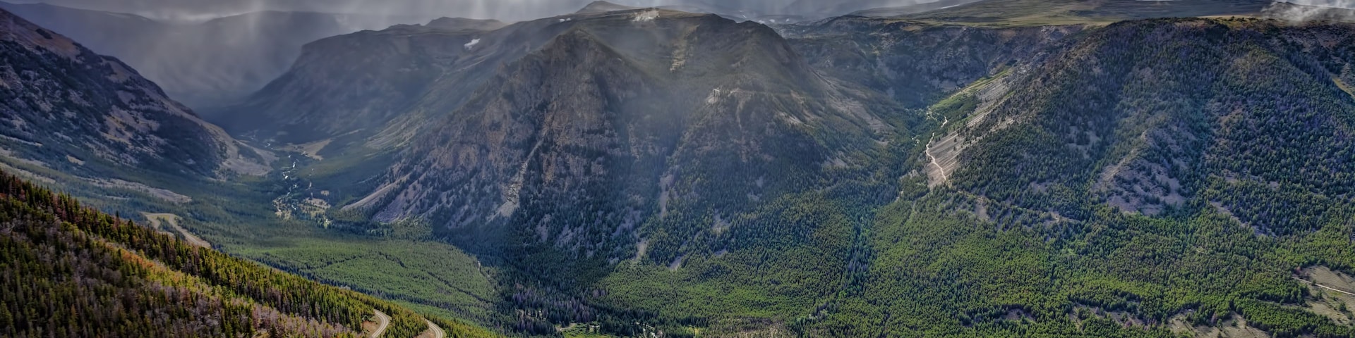 Eine gebirgige Landschaft mit einer kurvenreichen Straße, die durch einen dichten Wald führt.