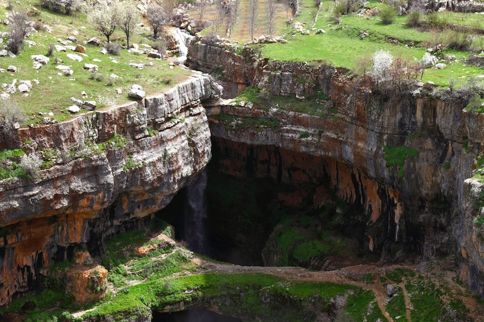 A large gorge with a waterfall, green vegetation, and terraced fields.