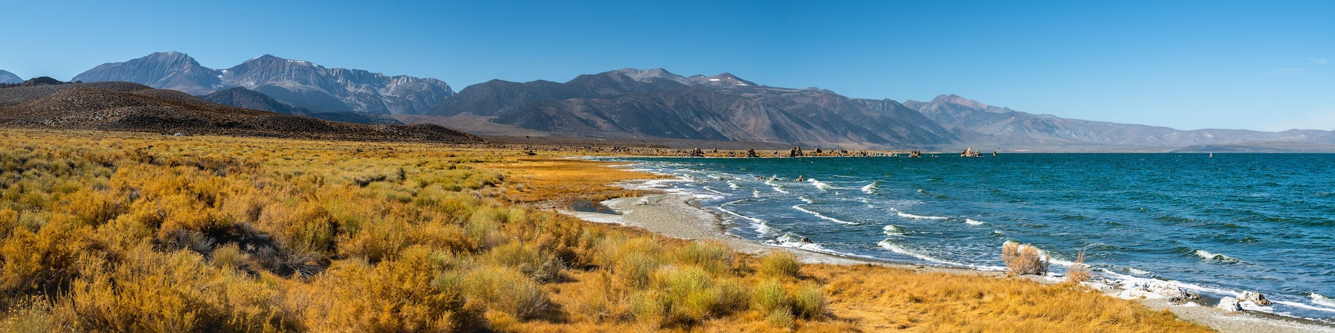 A coastal landscape with dry grass, a beach, and mountains in the background.