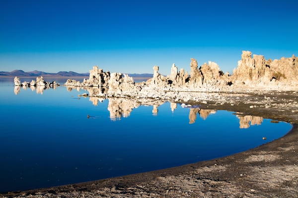 A calm lake with unique rock formations reflecting in the water, surrounded by a clear blue sky.