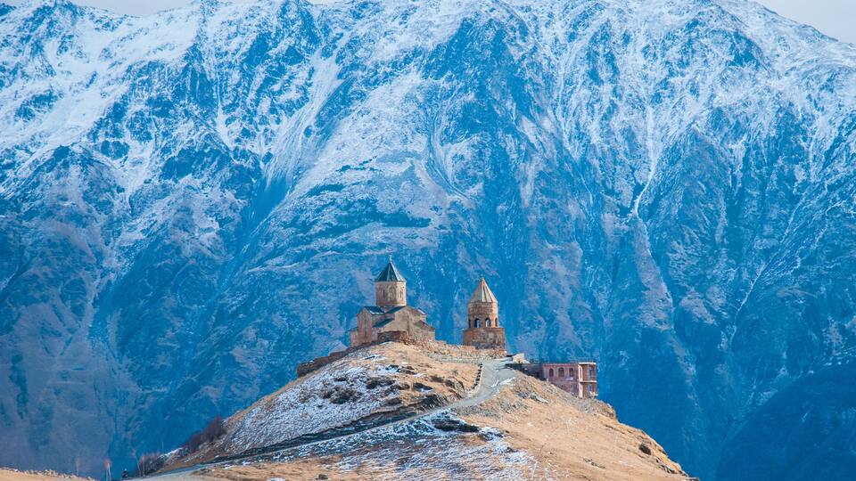 A snow-covered mountain with two small towers and a building on a hill.