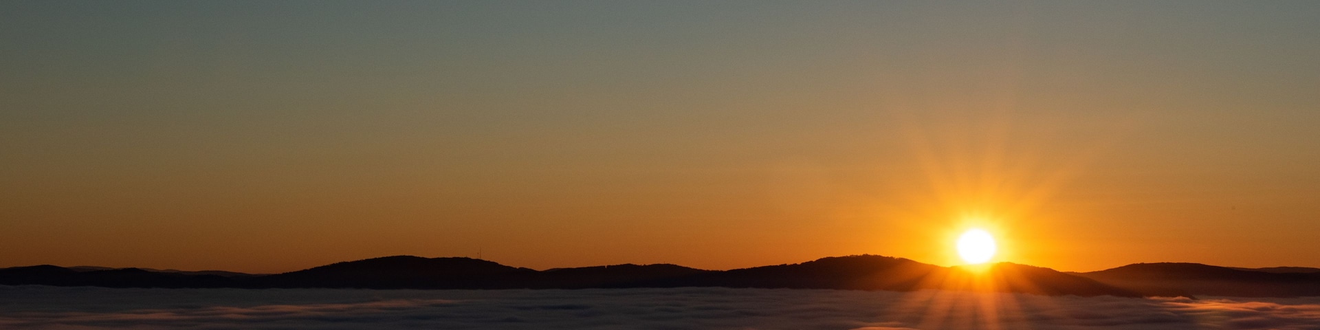 Un lever de soleil sur une chaîne de montagnes, avec des nuages en contrebas.