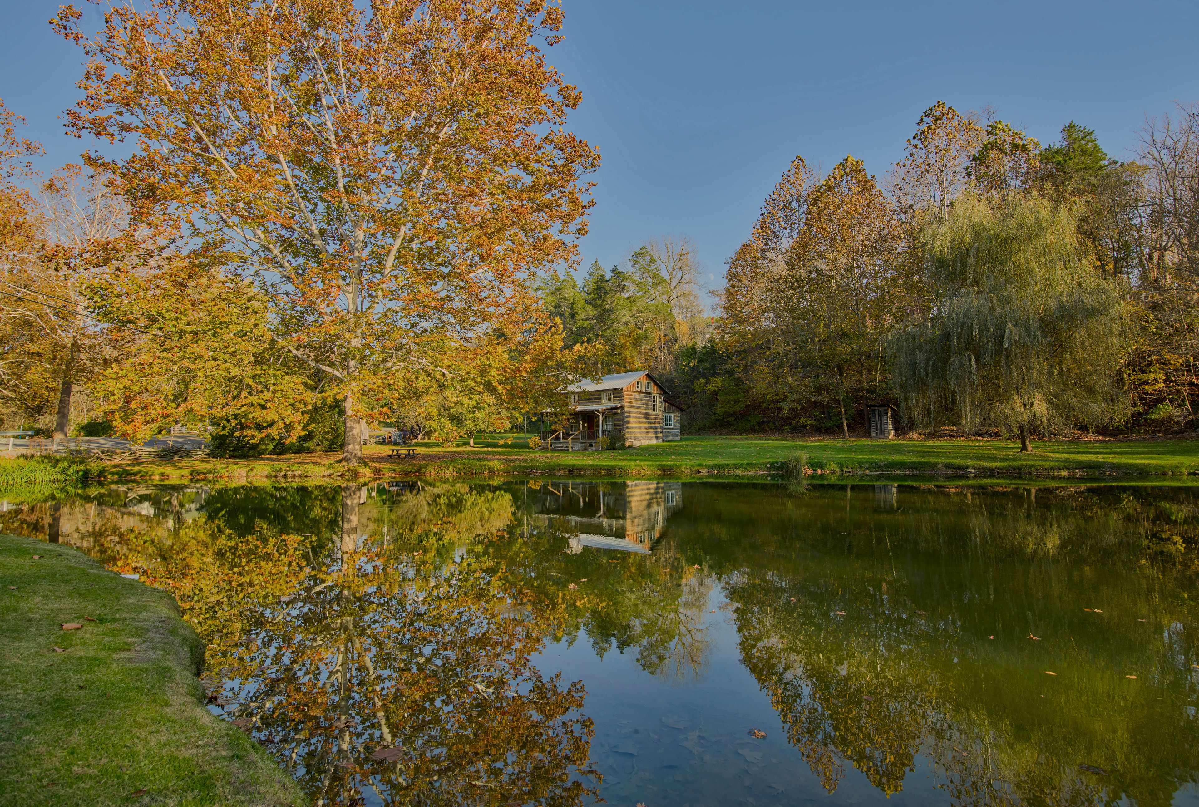 A serene lakeside scene with autumn foliage, a wooden cabin, and a clear reflection in the water.