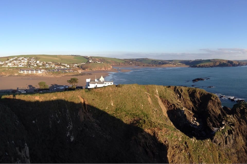 A coastal town with a prominent cliff, a beach, and a white building with a tower.