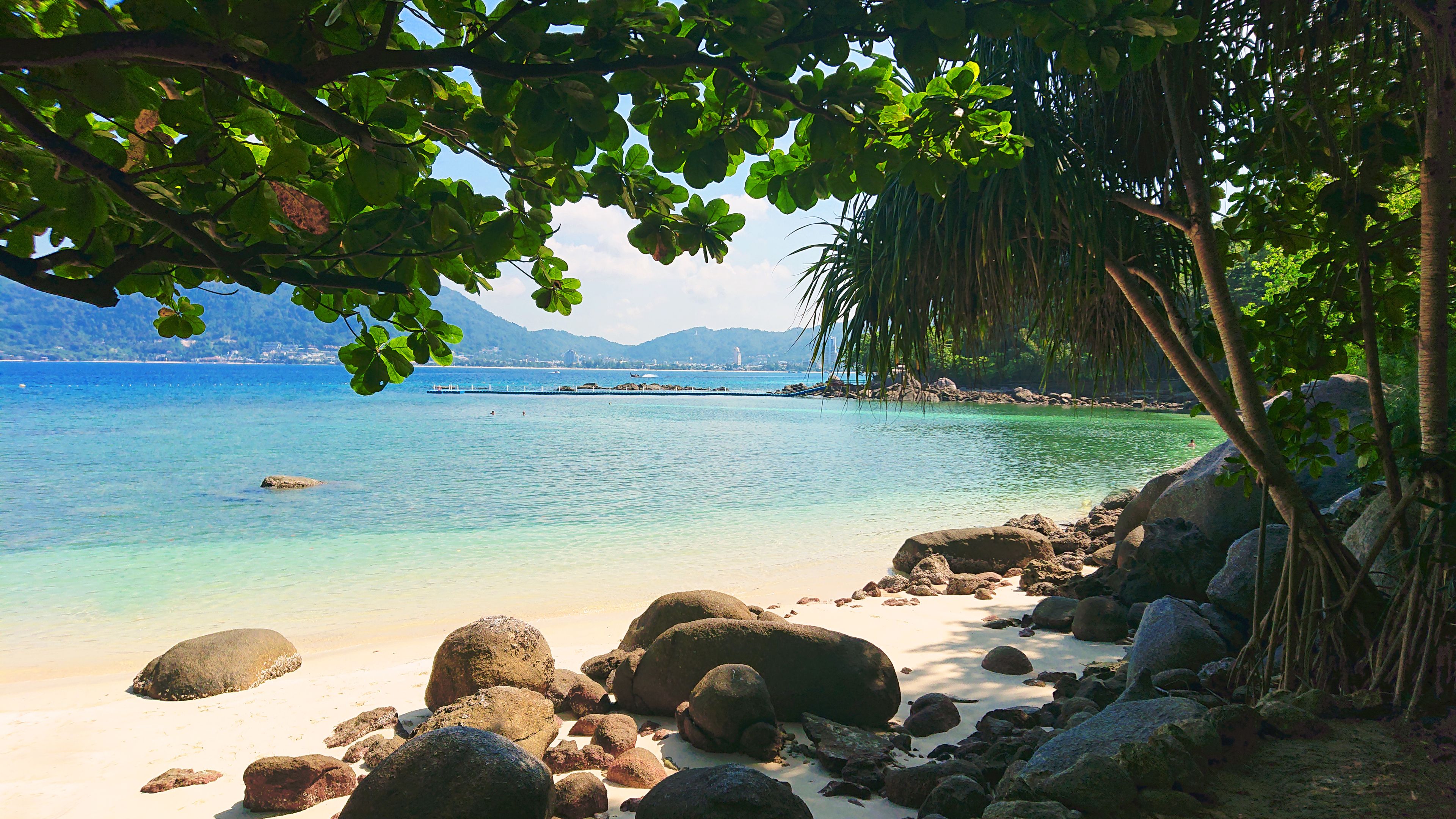 A tropical beach with clear turquoise water, large rocks, and lush greenery.