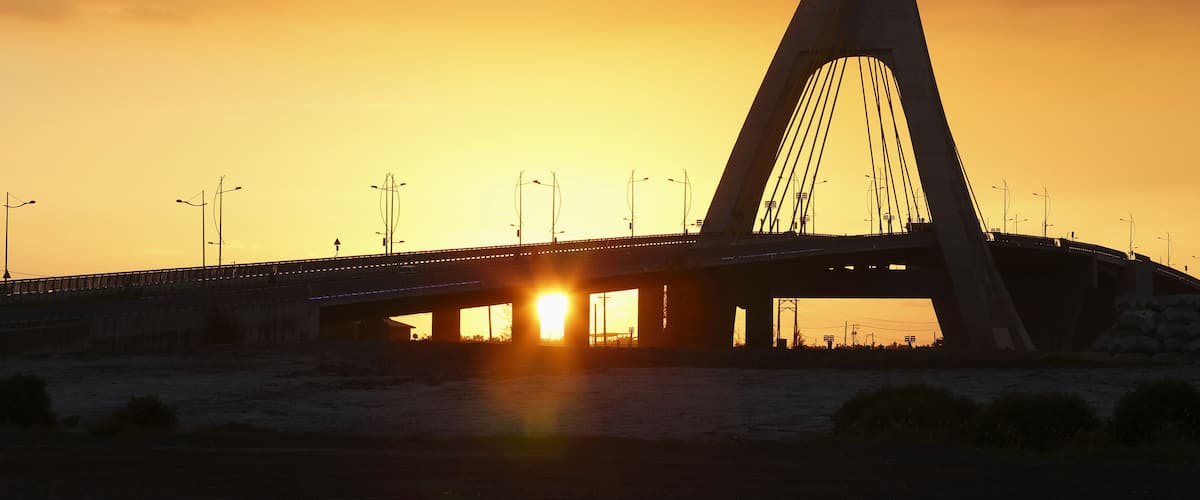 A bridge with a triangular arch silhouetted against a sunset sky.