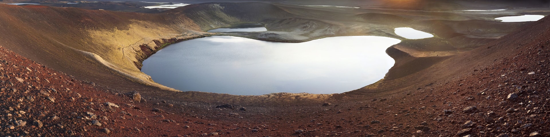 View of a serene lake nestled within a volcanic crater, its still waters reflecting the soft glow of the setting sun, Veidivotn, Rangárþing ytra, Iceland.