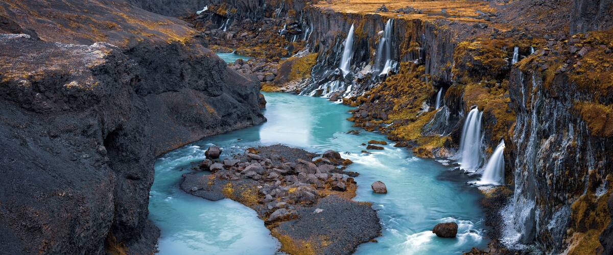 A river with multiple waterfalls flowing through a rugged landscape.